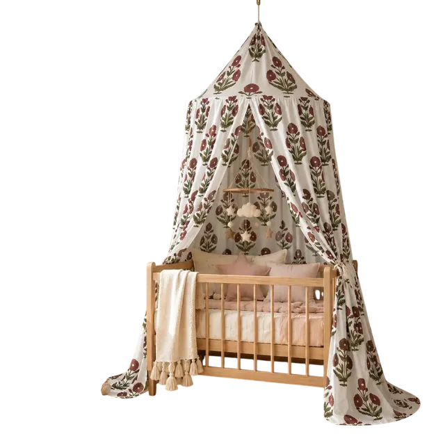 Red floral cotton canopy hanging over a wooden baby crib, featuring hand block printed flowers, gathered panels, cozy nursery decor